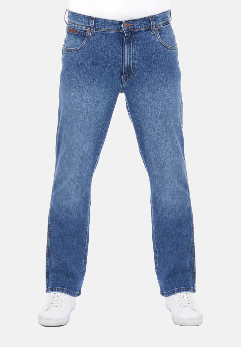 Jeans de denim azul claro con corte recto, cinco bolsillos, detalles de costura y cierre de botón. Llevados con zapatillas blancas.