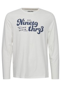 Langærmet hvid T-shirt lavet af bomuld med rund halsudskæring, der har et marineblåt grafisk tekstdesign på fronten.