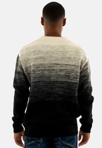 Suéter de punto con un degradado ombré que va de crema en la parte superior a negro en la parte inferior. Cuello y puños acanalados, con una textura suave en todo su alrededor.