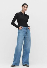 Musta ribattava pitkähihainen golfpaita, jossa on nappiyksityiskohta, yhdistettynä vaaleansinisiin leveälahkeisiin farkkuihin, joissa on nyöri vyötäröllä ja rento istuvuus.