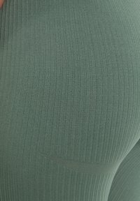 Collant verdi a coste e texture, realizzati in tessuto elasticizzato; presentano un design elegante con un accento sottile lungo la cucitura laterale.