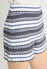 Shorts rayés en blanc, bleu et noir, présentant des lignes horizontales et un tissu texturé. Des fentes latérales améliorent le confort et l'ajustement.