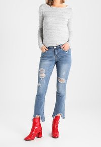 Szary, długi rękaw, jasnoniebieskie, postrzępione dżinsy z wykończeniem na brzegach oraz błyszczące, czerwone botki na kostkę z grubym obcasem.