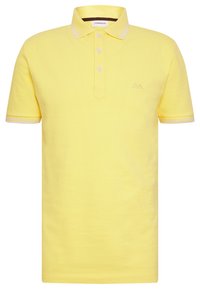 Keltainen polo-paita klassisella kauluksella, jossa on kolme nappia ja valkoiset korostusraita hihassa. Paidassa on pieni brodeerattu logo rinnan kohdalla.