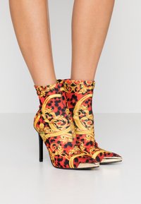 Stivali alla caviglia con stampa leopardata rossa e nera, decorati con motivi barocchi dorati, punta affusolata e tacco a spillo. Materiale morbido e elastico.