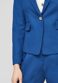 Blå skräddarsydd blazer i slätt tyg, med två framfickor, enkel knäppning och långa ärmar; kombinerad med matchande byxor.