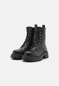 Cizme de ankle negre cu șireturi, realizate din piele texturată, cu o talpă chunky și adâncită, având gauri metalice pentru șireturi.