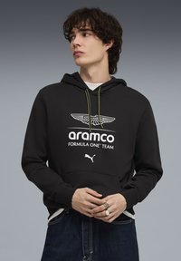 Sweat à capuche noir avec une poche kangourou à l'avant, arborant le logo blanc d'Aston Martin et le texte "aramco FORMULA ONE™ TEAM", avec des cordons néon jaunes.