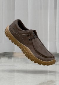 Zapato slip-on de ante marrón con suela de goma texturizada, que presenta un diseño minimalista y cordones elásticos para un uso fácil.