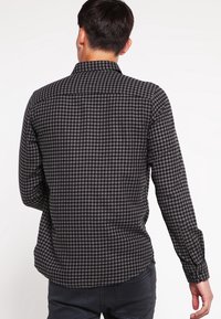 Musta- ja harmaaruudullinen pitkähihaisen paita, jossa on napillinen kaulus ja suora selkäosa. Vakiomallinen istuvuus ja pehmeä kangas.