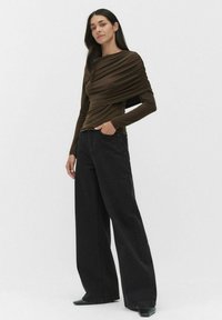 Ruskea, pitkähihaisessa paidassa on roikkuva pinta ja tiukka vartalo. Yhdistetty korkeavyötäröisiin mustiin leveälahkeisiin farkkuihin, joissa on vaaleita pilkkuja.