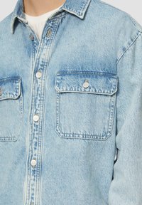 Jasnoniebieska koszula z denimu z klasycznym kołnierzykiem, dwoma kieszeniami na piersiach, srebrnymi guzikami oraz wyblakłą fakturą z subtelnymi przetarciami.