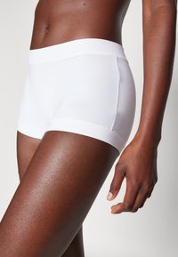 White cotton boxer shorts with a smooth texture and elastic waistband, featuring a snug fit that extends to mid-thigh.