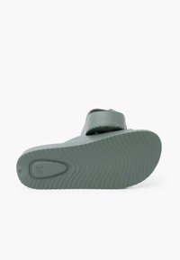 Sandale en caoutchouc verte avec une surface texturée, une large sangle, et une semelle flexible avec un motif de bande de roulement nervuré et un marquage de taille.