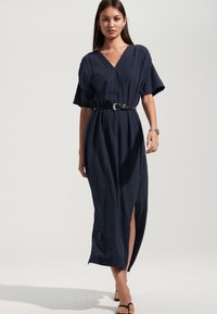 Tumši zila maxi kleita ar īsām piedurknēm, V veida izgriezumu, jostu viduklī un sānu šķēlumu, izgatavota no viegla auduma ar smalku tekstūru.