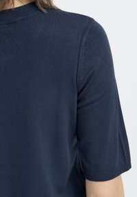 Tengerészkék kötött pulóver kerek nyakkivágással és rövid ujjakkal. A szövet sima tapintású, a gallérnál és a mandzsettánál finom bordázattal díszített.