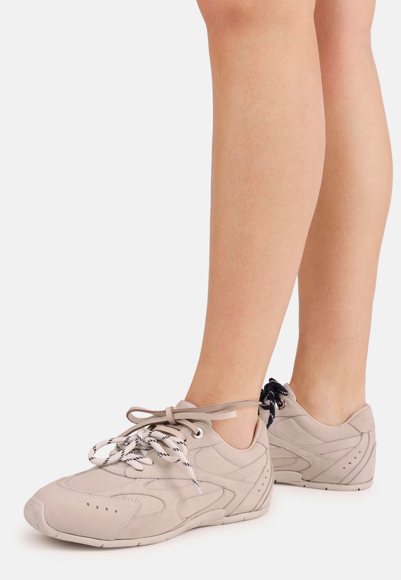 Ανοιχτόγκρι αθλητικά παπούτσια με υφή σουέτ, διακοσμημένα με αντίθετα κορδόνια, στρογγυλεμένο σχήμα και διακριτικές πλευρικές λεπτομέρειες.