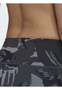 I pantaloni corti atletici grigi in camouflage presentano una vita aderente con accenti a strisce bianche e nere e una texture di tessuto liscia e elastica.
