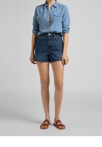 Světle modrá košile na knoflíky s dvěma náprsními kapsami, v kombinaci s tmavými džíny s vysokým pasem a hnědými sandály se dvěma popruhy.