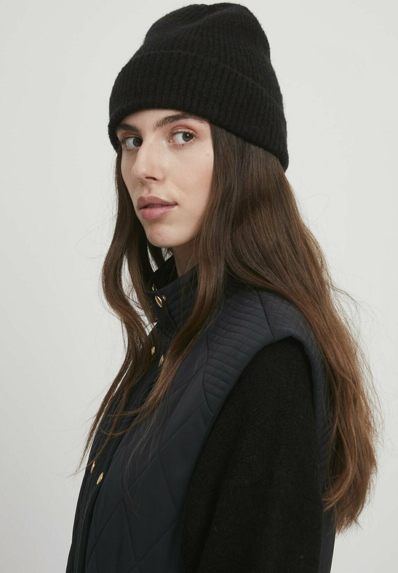 Beanie in maglia nera e gilet trapuntato blu notte con bottoni dorati, caratterizzato da un colletto alto e design senza maniche. Texture liscia e silhouette aderente.