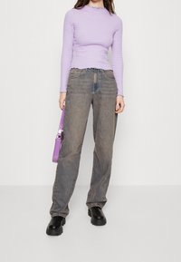 Długi rękaw w paski w kolorze fioletowym i białym z falbankowymi krawędziami, zestawiony z wysokim stanem wyblakłych niebieskich dżinsów i czarnymi masywnymi butami.