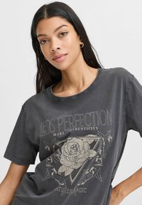 Grå t-shirt lavet af bomuld med en afslappet pasform, der har et stort rosenmotiv og tekstprint i cremede farver. Kortærmet og med rund halsudskæring.
