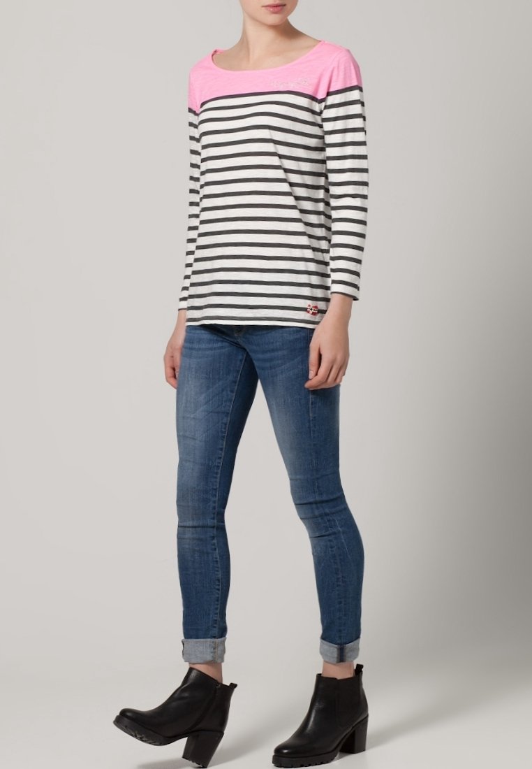Striped long-sleeve shirt featuring a pink neckline, gray and white stripes, and a small logo detail at the hem, worn with blue jeans and black boots.