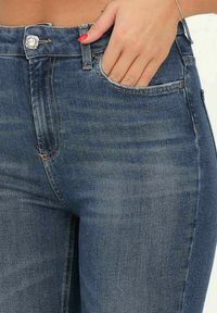 Jeans in denim blu scuro con vita media, dotati di un bottone decorato con gemme, tasca frontale e dettagli di scolorimento sottili sul tessuto.