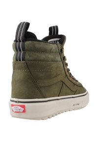 Zapatillas altas en ante verde oliva con suela blanca de goma, que cuentan con ojales de metal, un acento de rayas en blanco y negro, y un parche de logo.