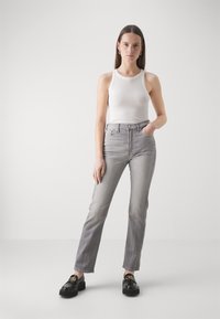 Jeans grises de cintura alta con corte recto y acabado desteñido. Combinados con una camiseta de tirantes blanca de canalé y mocasines negros con herrajes dorados.