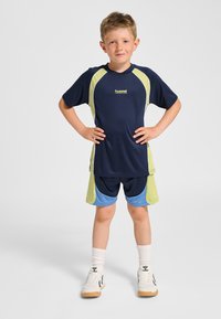 Marinblå och limegrön sporttröja med korta ärmar, kombinerad med blå och gröna shorts. Bärs med vita strumpor och vita sneakers.