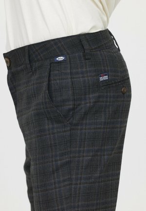 Pantalons à carreaux gris avec des accents bleus et jaunes, présentant des poches avant, une taille avec un bouton, et une étiquette sur le côté avant.