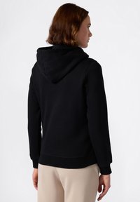 Sudadera negra con un ajuste relajado, textura suave y puños de canalé. Incluye una capucha ajustable con cordón y un dobladillo recto.