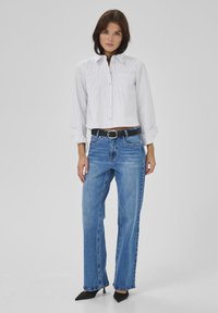 Camicia a righe bianche e grigie chiare con taschino, abbinata a jeans blu a gamba dritta e una cintura nera. Tacchi neri a punta.