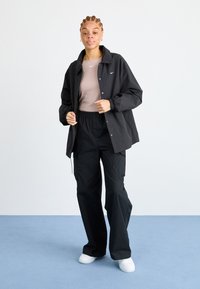 Juodas lengvas švarkas su apykakle, dėvimas ant bežinio marškinėlio ir derinamas su juodais kargo šortais. Balti sportbačiai užbaigia įvaizdį.