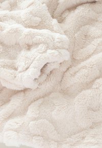 Jasnobeżowy pluszowy koc o miękkiej, teksturowanej powierzchni i subtelnym falistym wzorze, prezentujący przytulny, gruby materiał frotte.