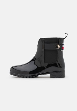Botte de pluie noire brillante à la cheville avec panneaux latéraux élastiques, sangle décorative avec bouton métallique, languette de tirage et talon bloc bas.