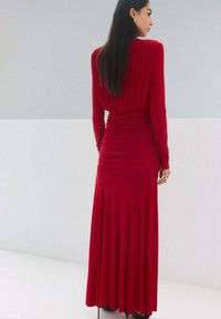 Rochie roșie cu mâneci lungi, cu corsaj adunat și fustă fluidă, realizată dintr-un material elastic, cu textură netedă și cădere elegantă.