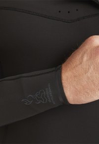Black wetsuit arm with smooth texture, featuring a logo in blue and a banded cuff for secure fit. Durable, made from recycled materials.