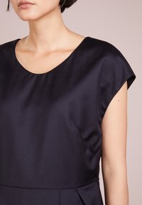 Námořnické modré saténové šaty s širokým výstřihem a krátkými rukávy. Mají volnou texturu a jemné záhyby v pase.