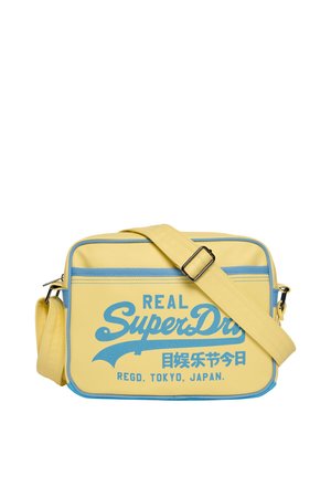 Yellow rectangular shoulder bag with blue trim and adjustable strap, featuring blue "Real SuperDry" text and Japanese characters on front.