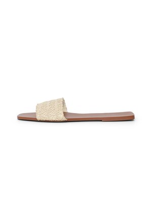 Des sandales plates avec une bride en tissu texturé blanc cassé et une semelle lisse couleur tan, au design minimaliste et sans ornement.
