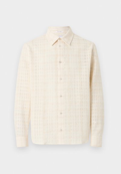 Κρεμ πουκάμισο με μακριά μανίκια και κουμπιά, με υφασμένο καρό μοτίβο, μυτερό γιακά και κουμπιά στο μπροστινό μέρος, εμφανίζεται σε απλό φόντο.