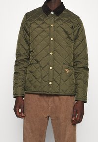 Vadderad grön jacka med brunt manchesterkrage, guldfärgade knappar och två framfickor. Har en liten logotyp på vänster bröst.