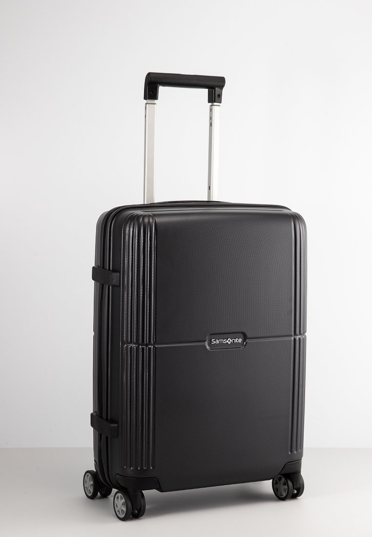 Black hard-shell suitcase with vertical ribbed texture, retractable handle, four wheels, and a Samsonite logo on the front.
