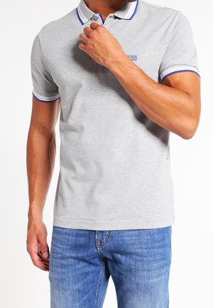 Camisa polo gris de manga corta con cuello, que presenta acentos de rayas azul y blanca, y un pequeño logo en el pecho. Etiqueta visible en la parte inferior.