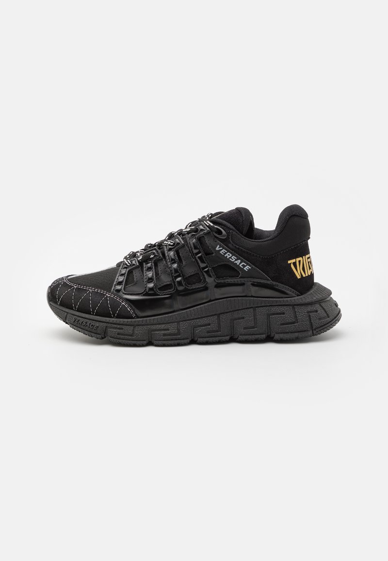 Black athletic sneaker with a textured upper, prominent lacing system, and rubber sole featuring a Greek key pattern. Accents include the brand logo.