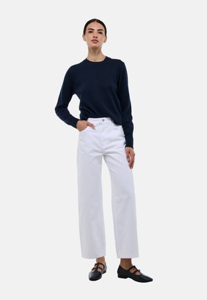 Pull en tricot marine, pantalon blanc à jambes larges et ballerines noires. Tissu texturé avec col rond, poches avant sur le pantalon, design minimaliste.