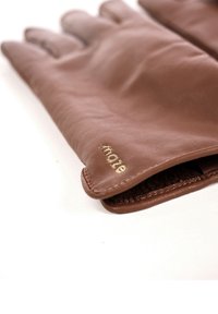 Brune læderhandsker med forstærkede syninger og en blød inderforing. Guldtekst "made" på manchet.