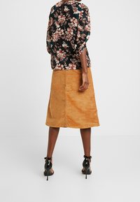 Bluzka w kwiatowy wzór z luźnymi rękawami, zestawiona z spódnicą z kordurowej tkaniny do kolan w ciepłym pomarańczowym kolorze, uzupełniona czarnymi sandałami na obcasie.